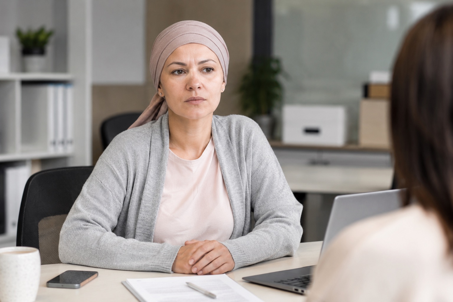 Mujer con pañuelo, superviviente de cáncer, en una reunión de trabajo frente a una mesa de oficina