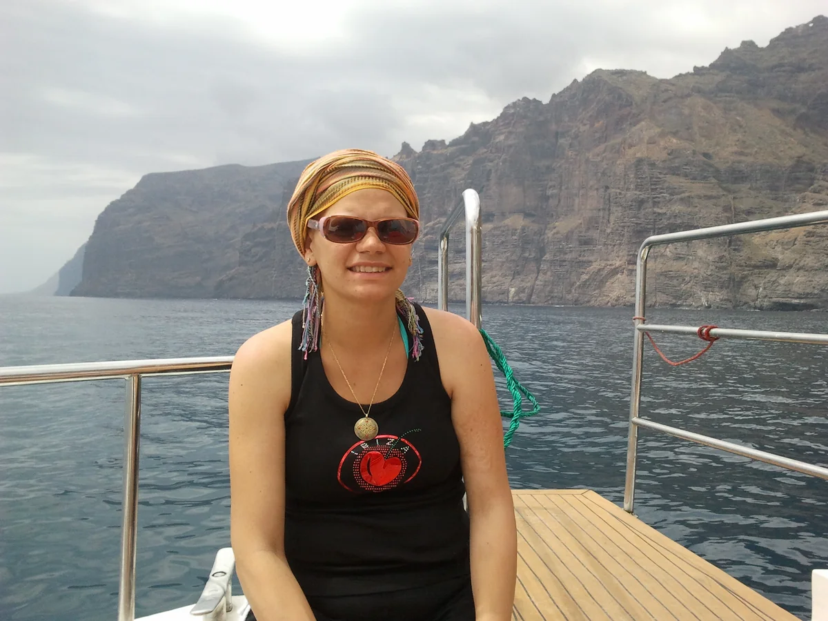Odile Fernández sonriente en un barco frente a unos acantilados en 2011, con pañuelo y gafas de sol durante la quimioterapia