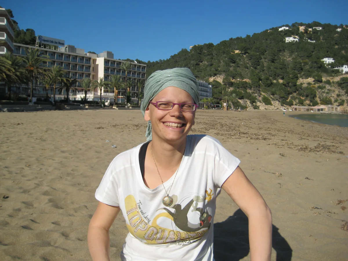 Odile Fernández en una playa de Ibiza en abril de 2011, con pañuelo en la cabeza, sonriendo durante el tratamiento